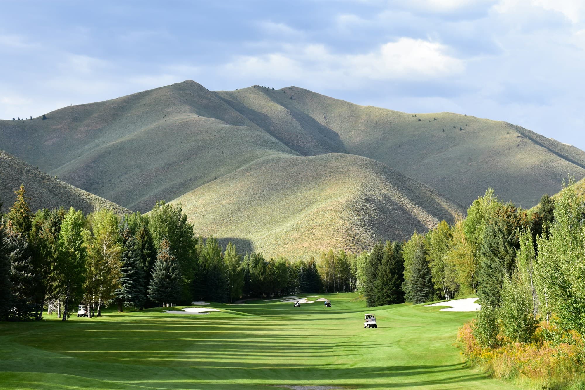 A sweeping sunlit golf course framed by rolling mountain ridges