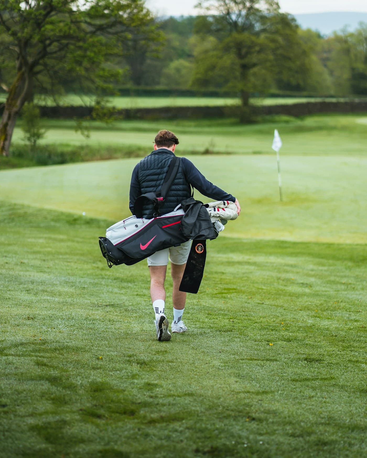 A player carrying his golf bag across a quiet fairway