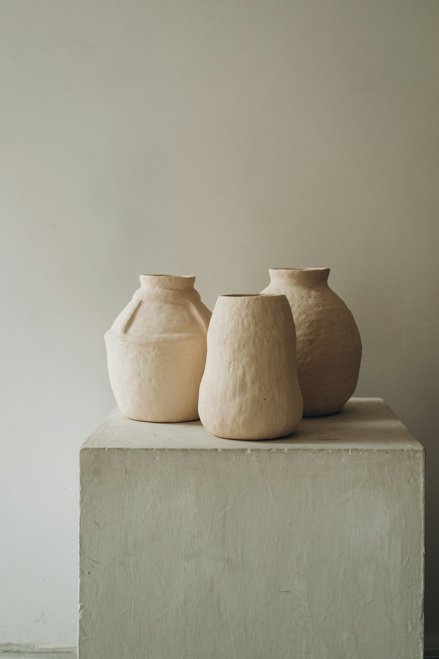 Three sculptural cream vessels on a pale pedestal